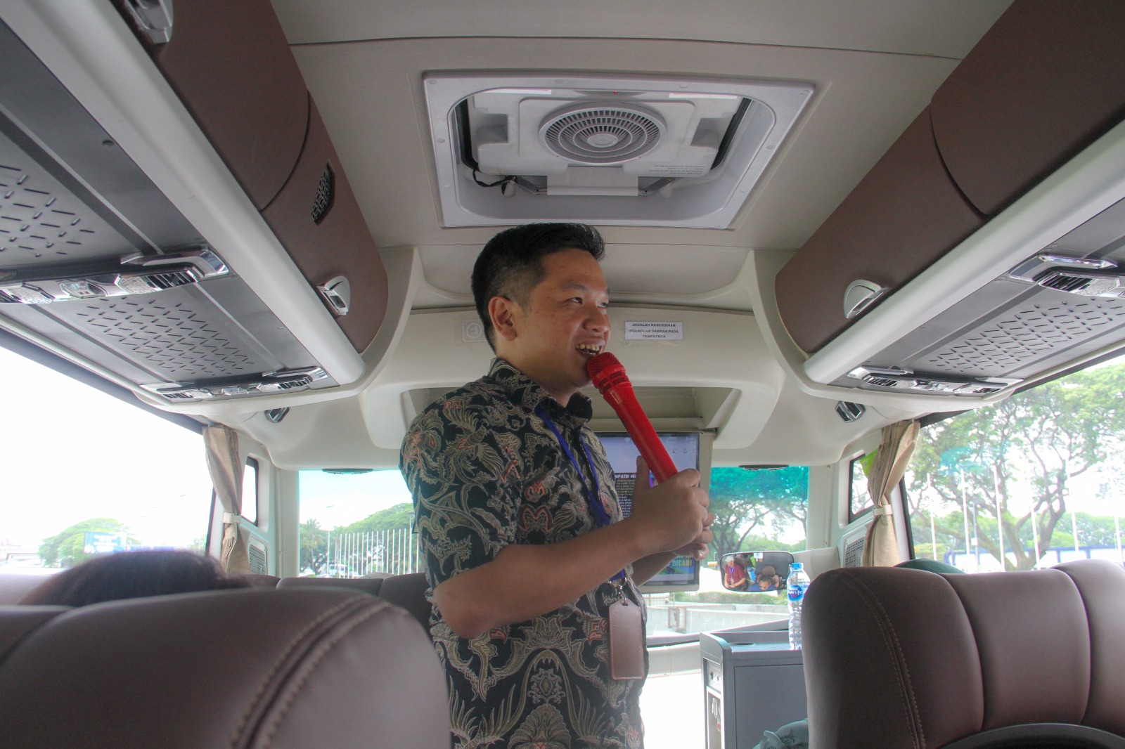 Smiling Indonesian male tour guide in traditional batik shirt pointing to mountain